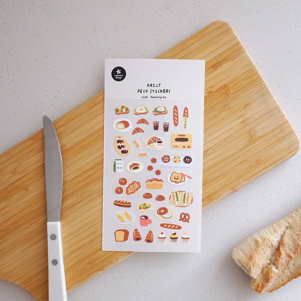 Sheet of food-themed Suatelier stickers on a wooden cutting board with a knife and bread.