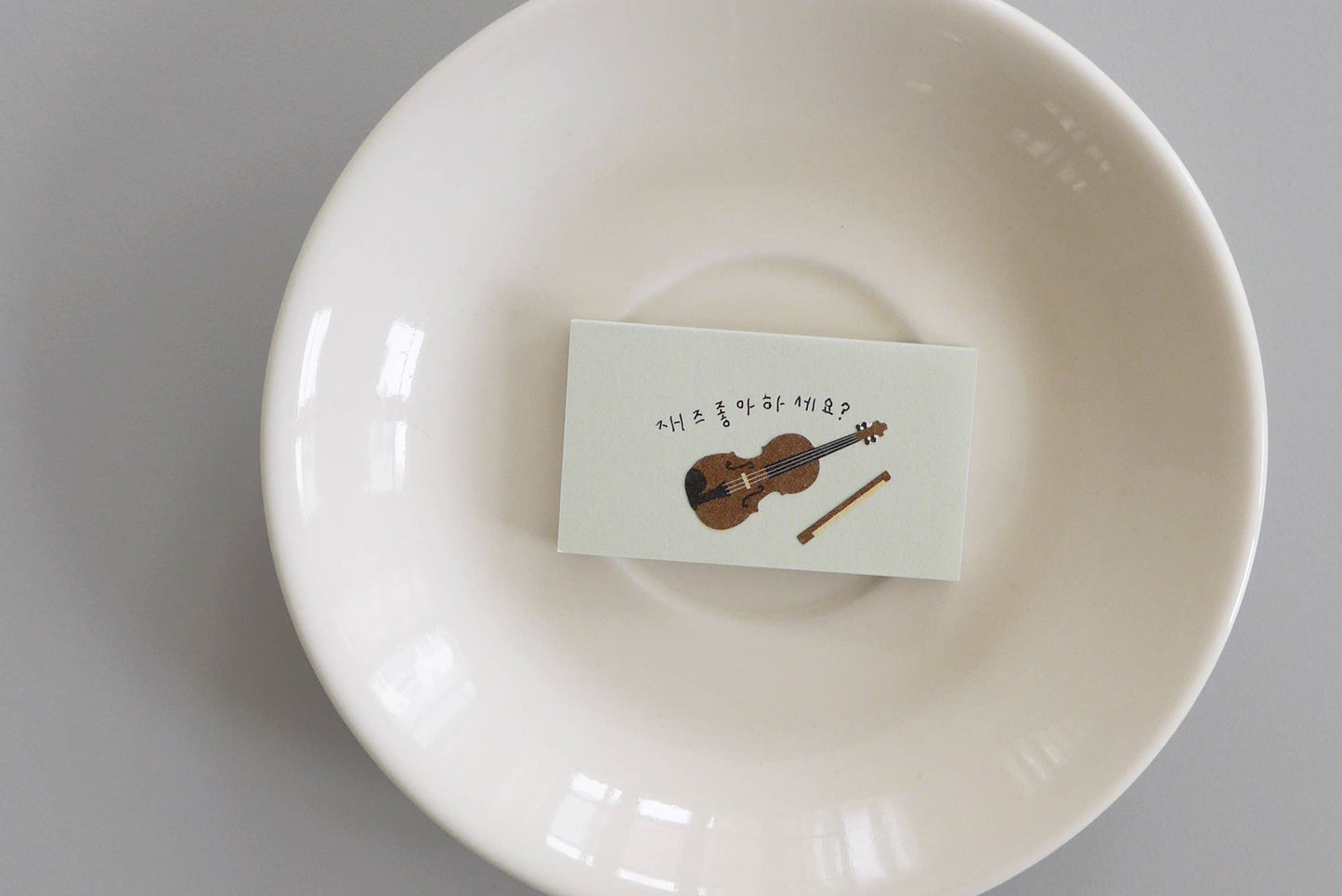White bowl with a card featuring a violin sticker by Suatelier on a gray background