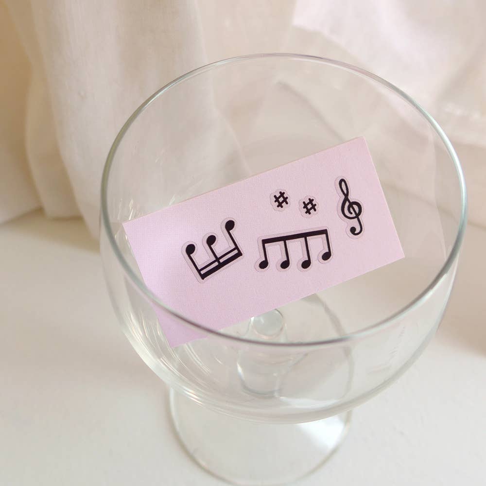 Clear glass with a pink card featuring musical symbols on a light background
