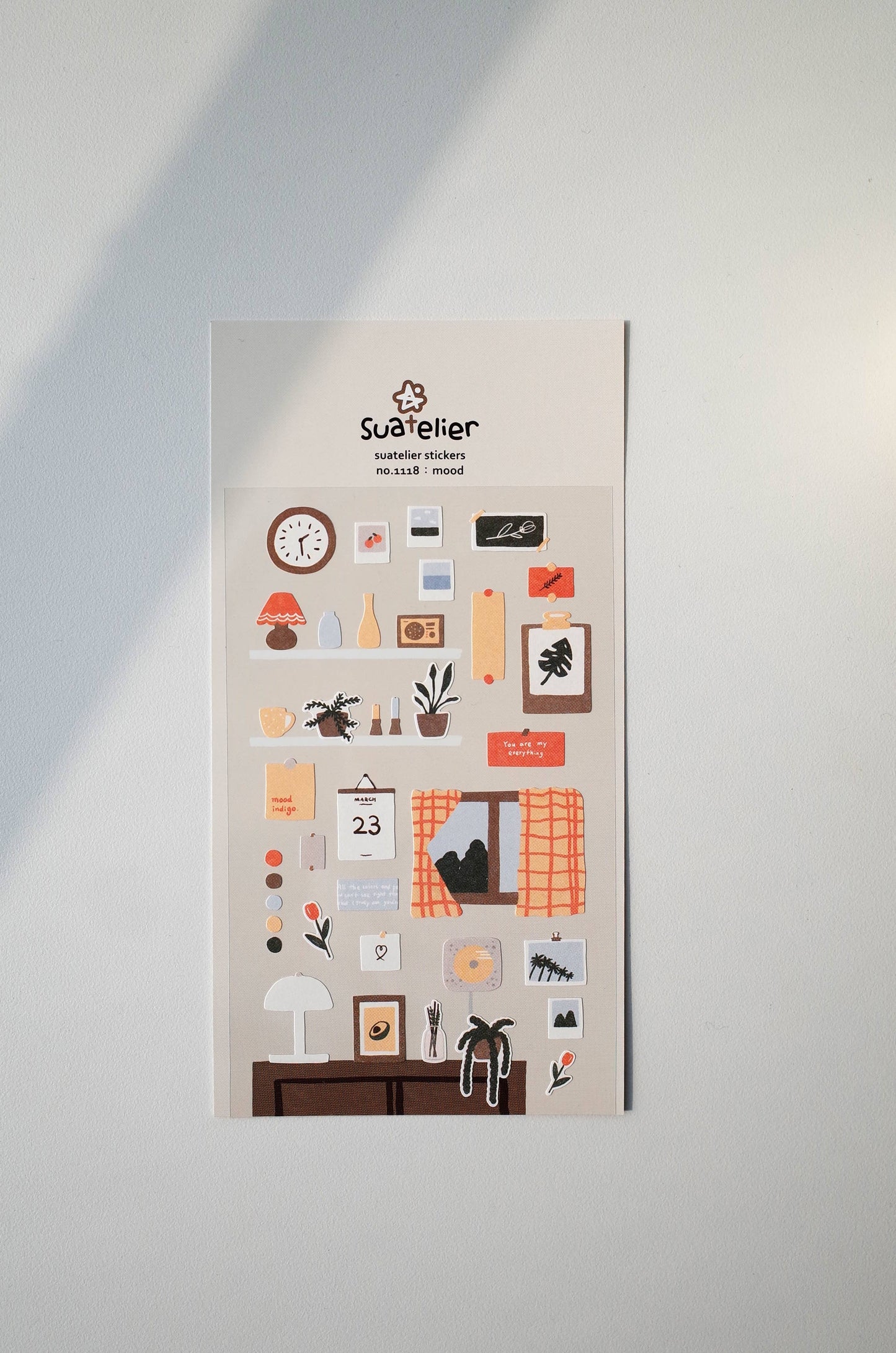 Suatelier sticker sheetnwith various icons and a brand logo on a light gray wall.