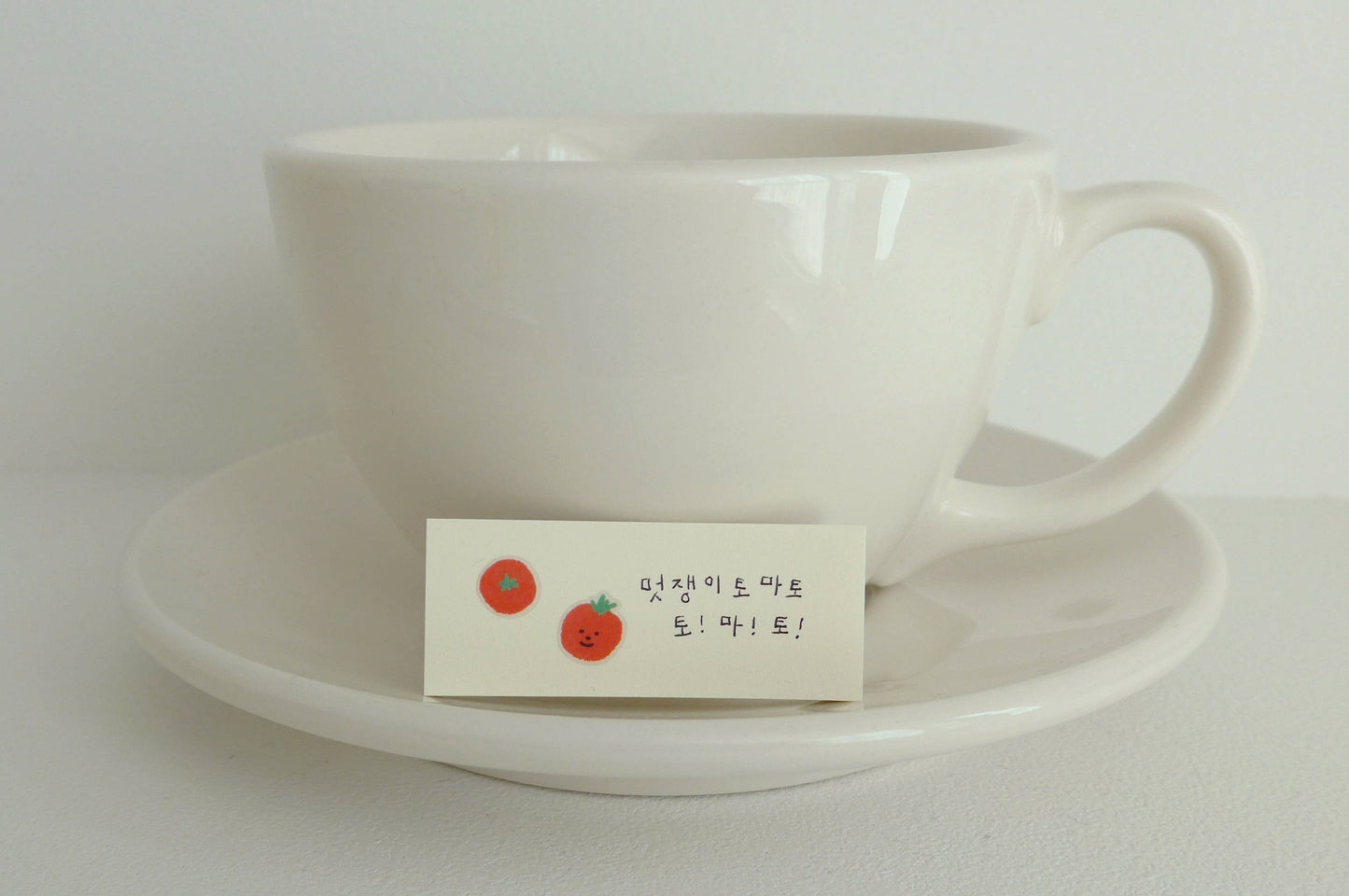 White ceramic cup and saucer with a small card featuring red tomatoes on a white background
