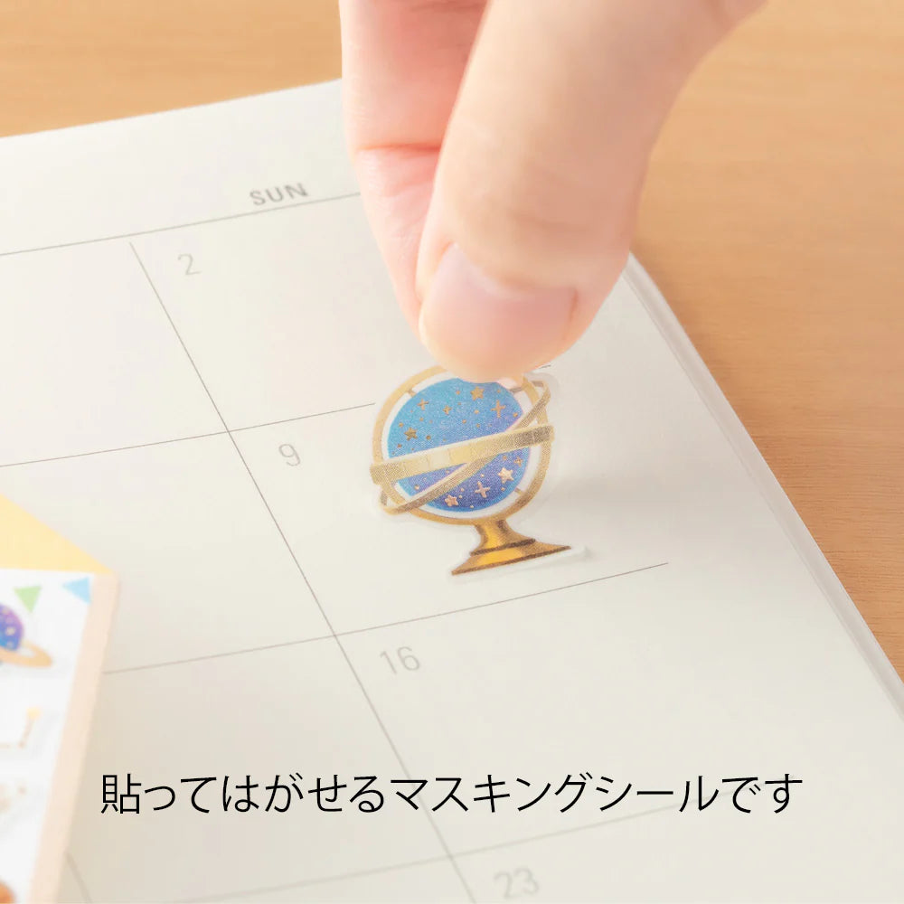 Hand applying a decorative masking seal by Midori with a globe design on a calendar.