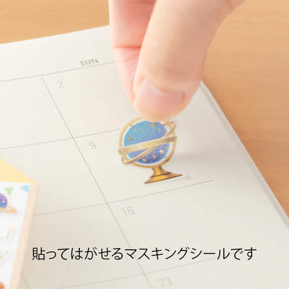 Hand applying a decorative masking seal by Midori with a globe design on a calendar.
